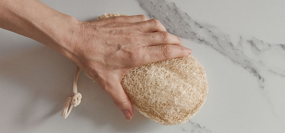 hand holding loofco bathroom cleaning loofah pad with marble tile background