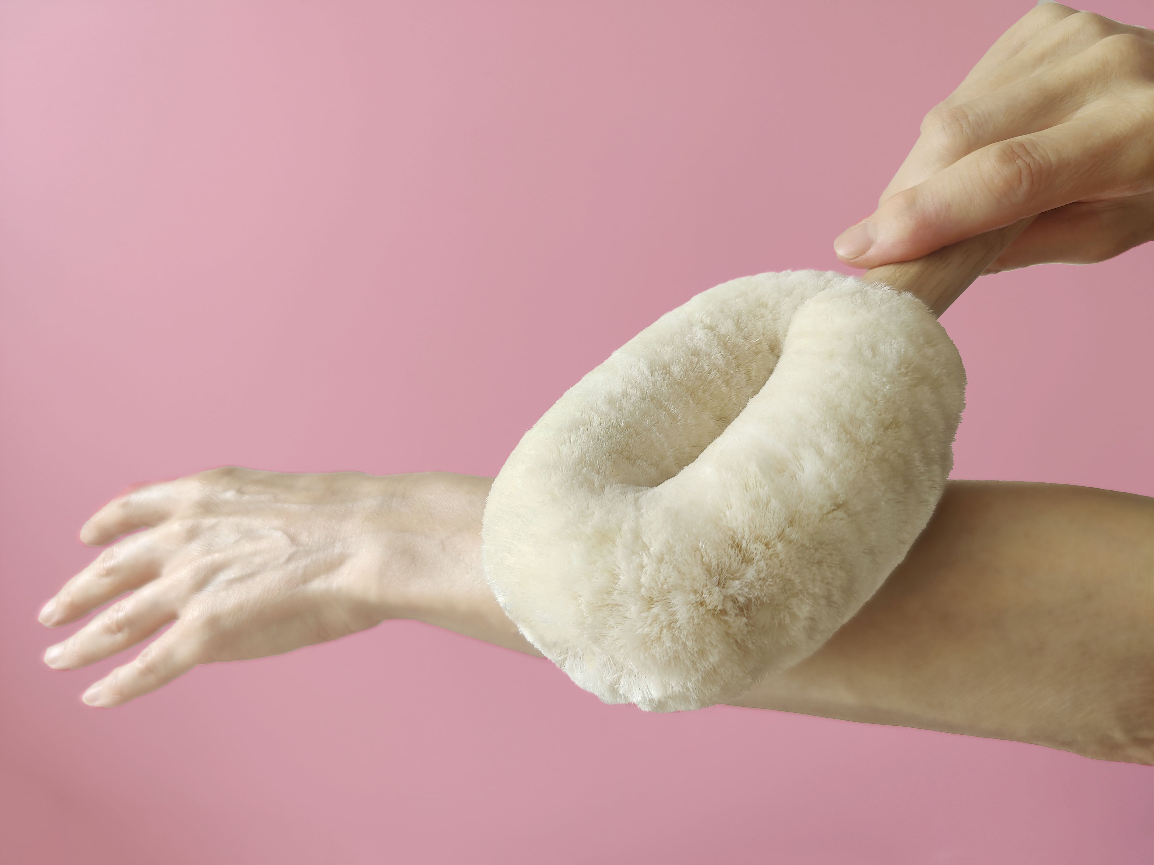 Hand holding a LoofCo Dry Body Brush against a pink background