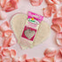Heart-shaped bath loofah with packaging on a bed of pink rose petals