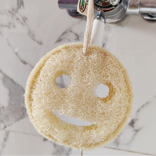 Smiley face LoofCo loofah hanging from a shower on a marble background