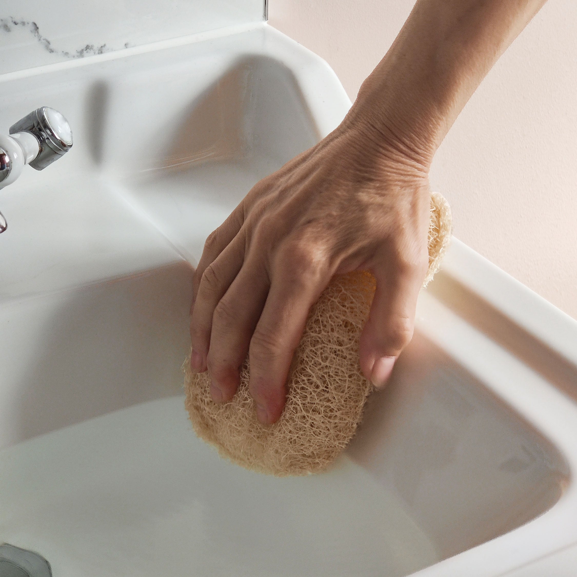 Hand holding a loofah sponge over a sink