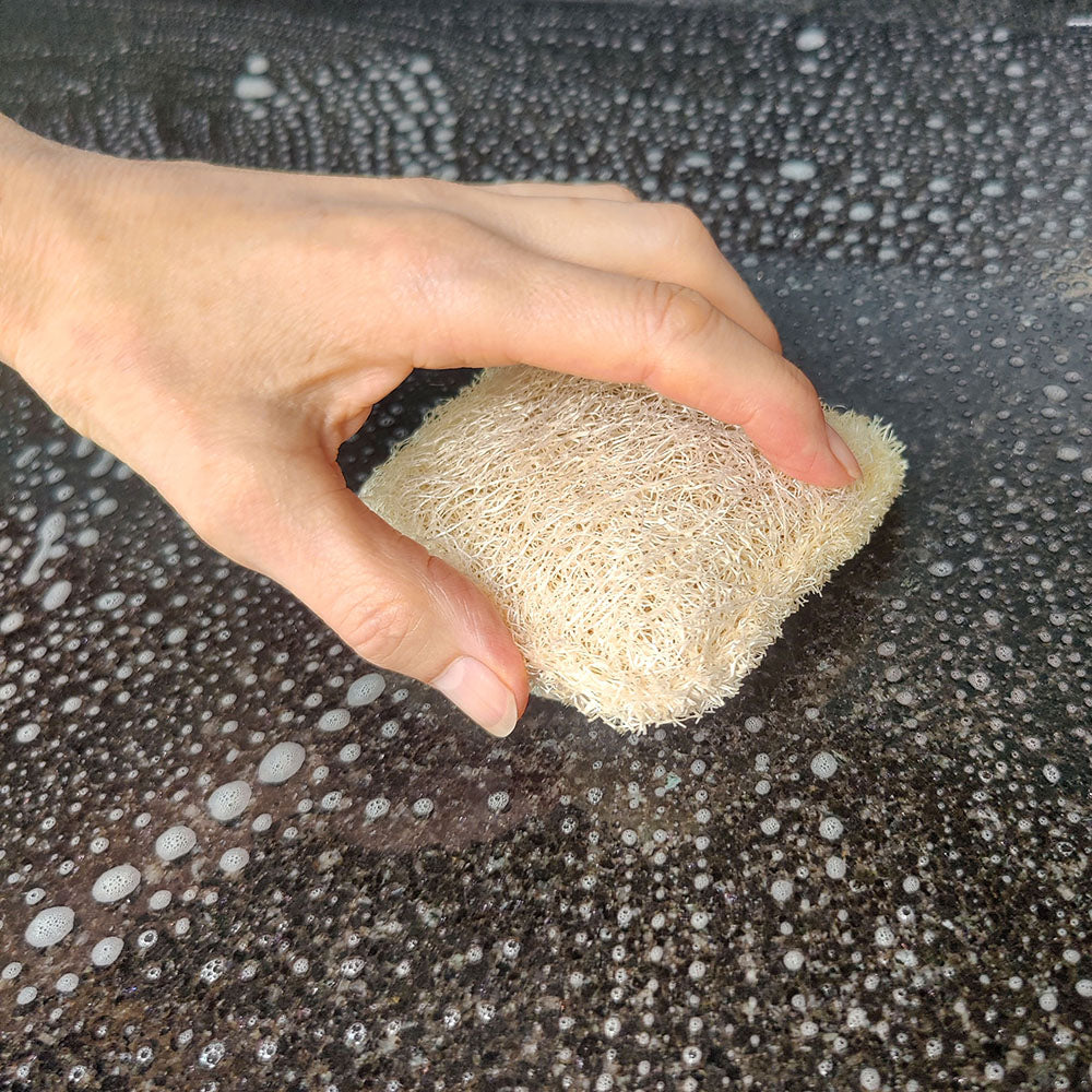 Hand holding a LoofCo Cleaning Pad loofah sponge over a soapy surface