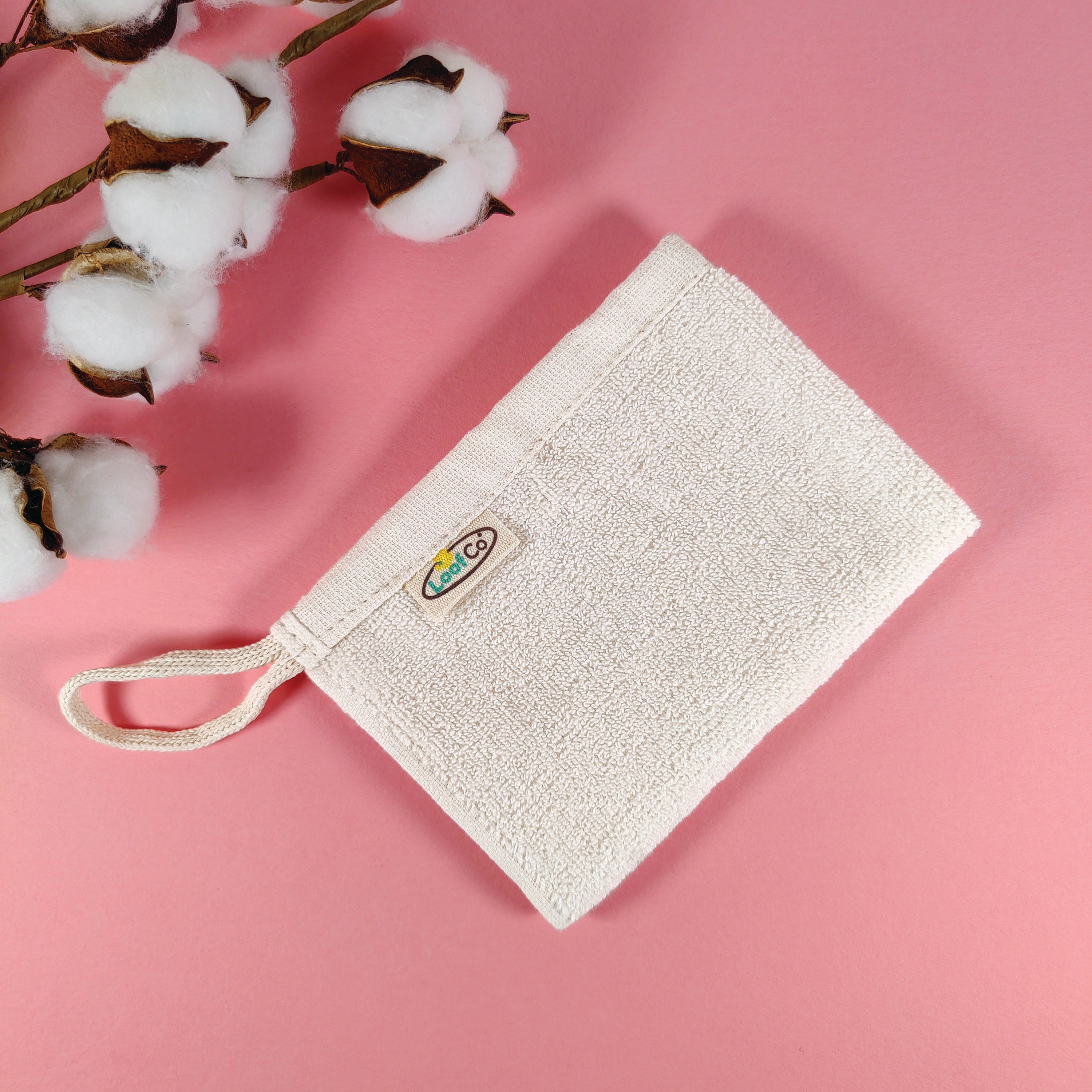 Folded LoofCo Kitchrn Cloth on a pink background with cotton flowers