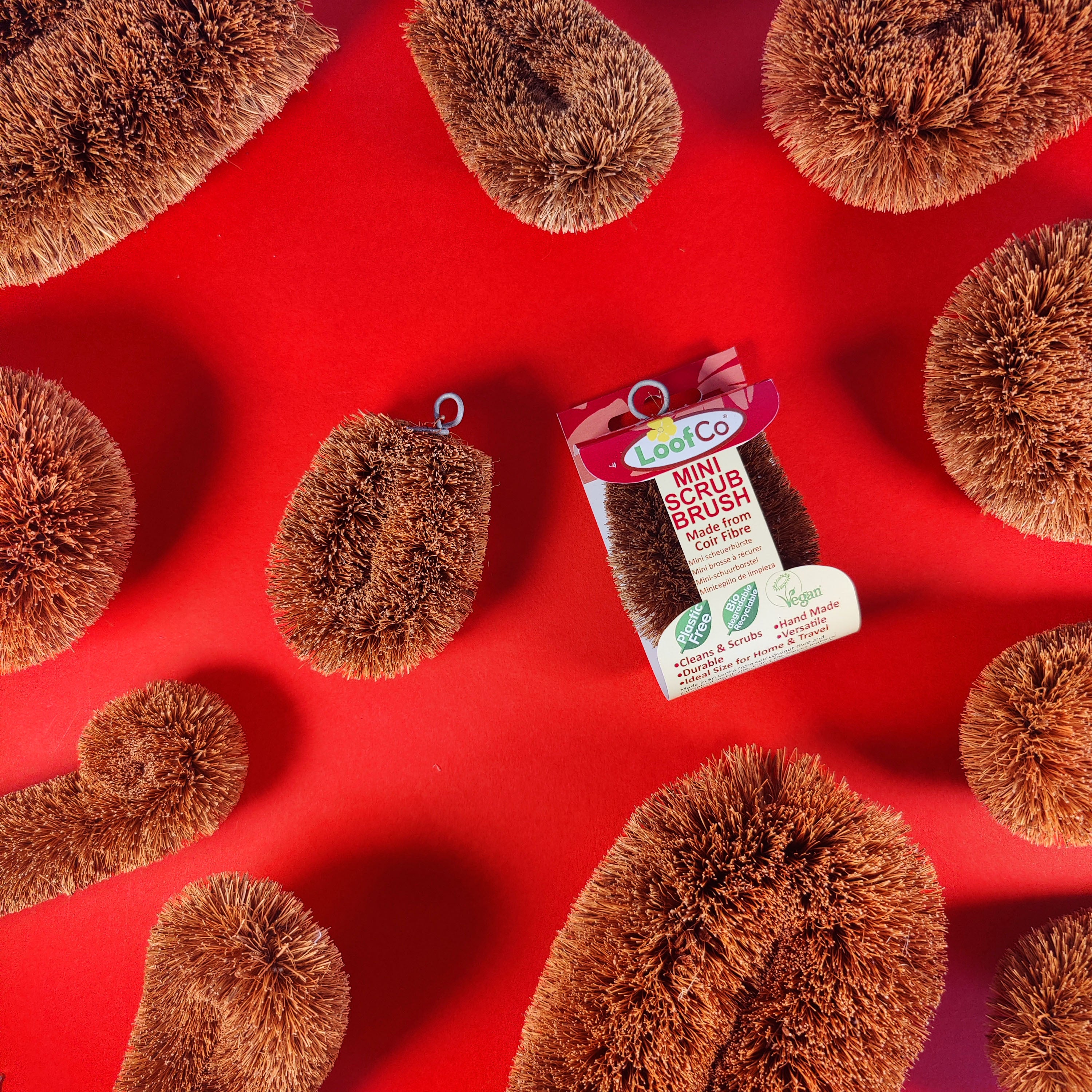 LoofCo mini scrub brush packaging on a red background with scattered brown scrubs.