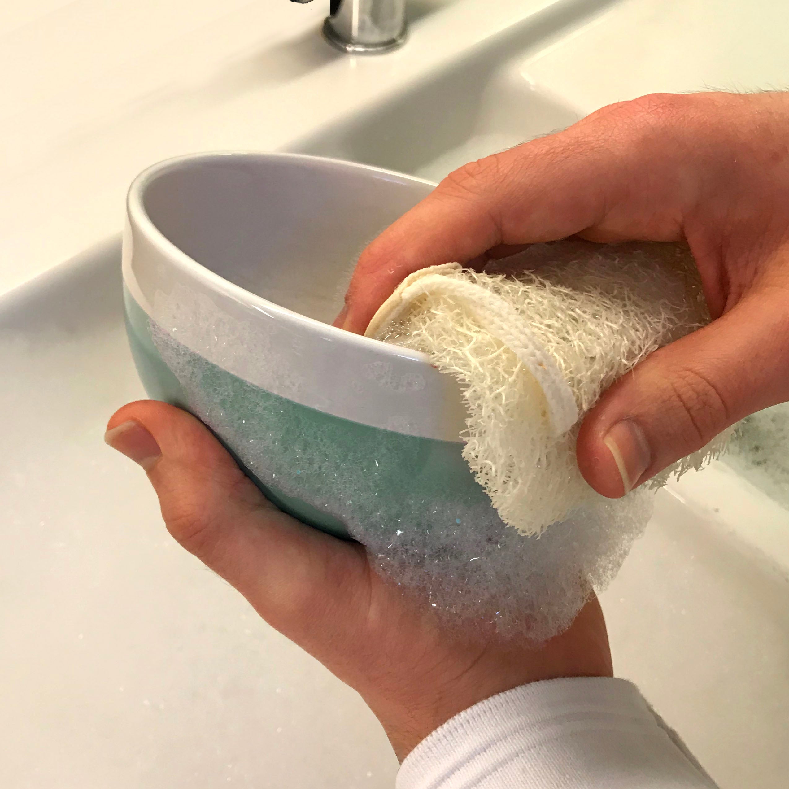 Person cleaning a blue bowl with a LoofCo Mini Washing-Up pad in front of a sink.