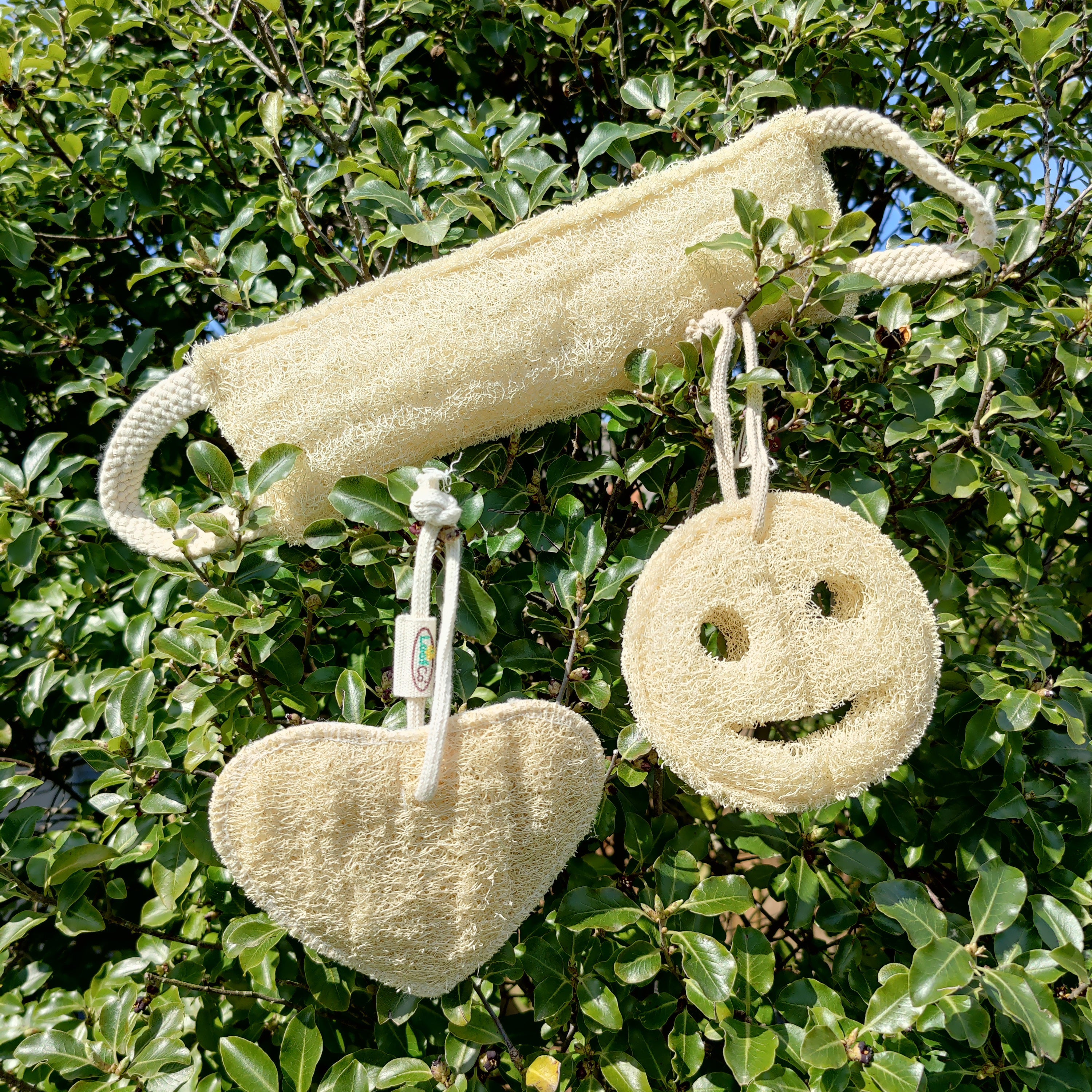 loofah back scrubber with a smiley face and heart shape loofah pads against a green leafy background