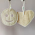 Two natural LoofCo loofahs, one round with a smiley face and one heart-shaped, hanging against a neutral background.