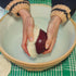 Person scrubbing a sweet potato with a Loofah root vegetable scrubber over a  bowl on a green checked tablecloth.