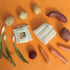 Assorted vegetables including potatoes, carrots, and onions on an orange background with LofCo loofah Root Vegetable Scrubbers.