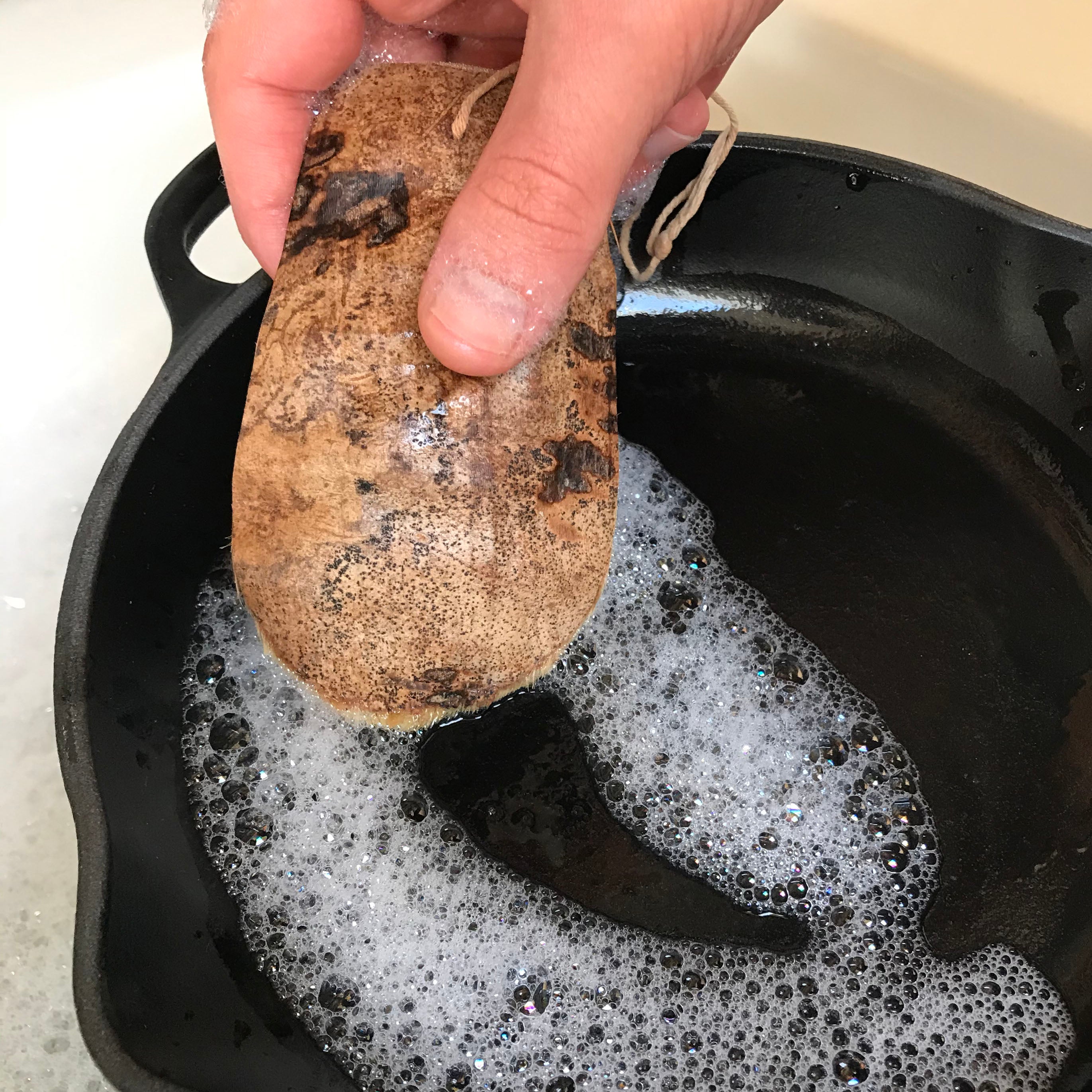 Person scrubbing a cast iron skillet with a coconut husk Washing-Up Scraper.