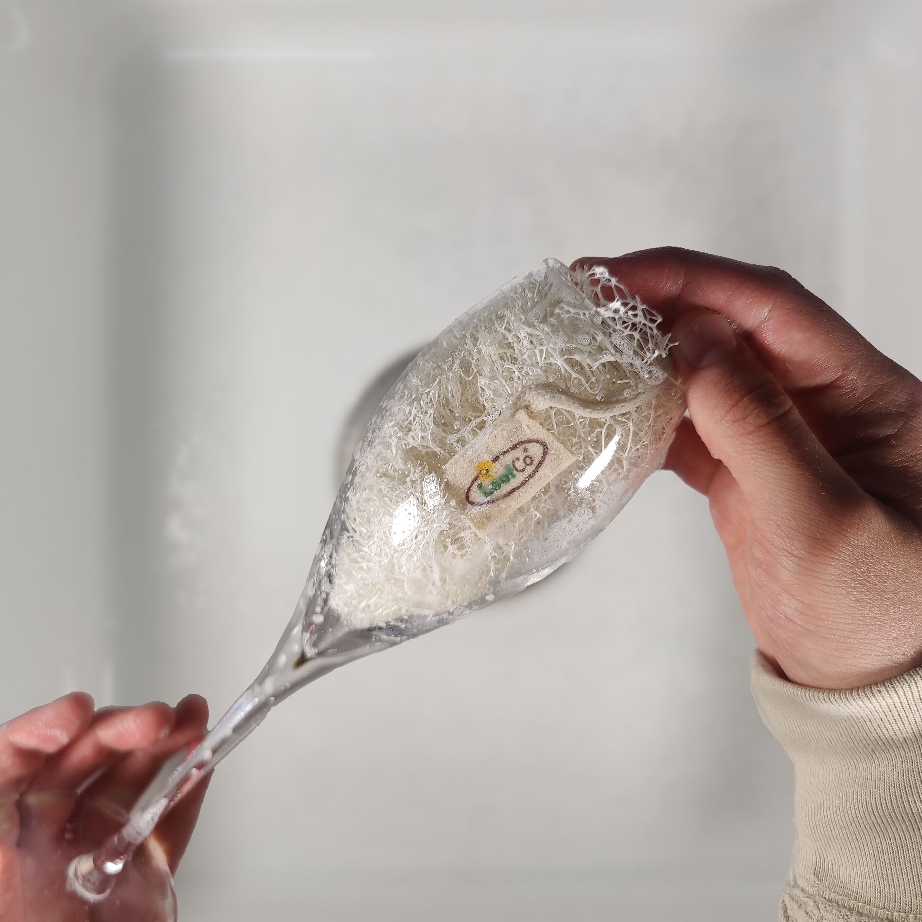 2 hands using LoofCo Washing-Up Slim Pad to clean a champagne glass against a neutral background