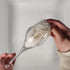 2 hands using LoofCo Washing-Up Slim Pad to clean a champagne glass against a neutral background