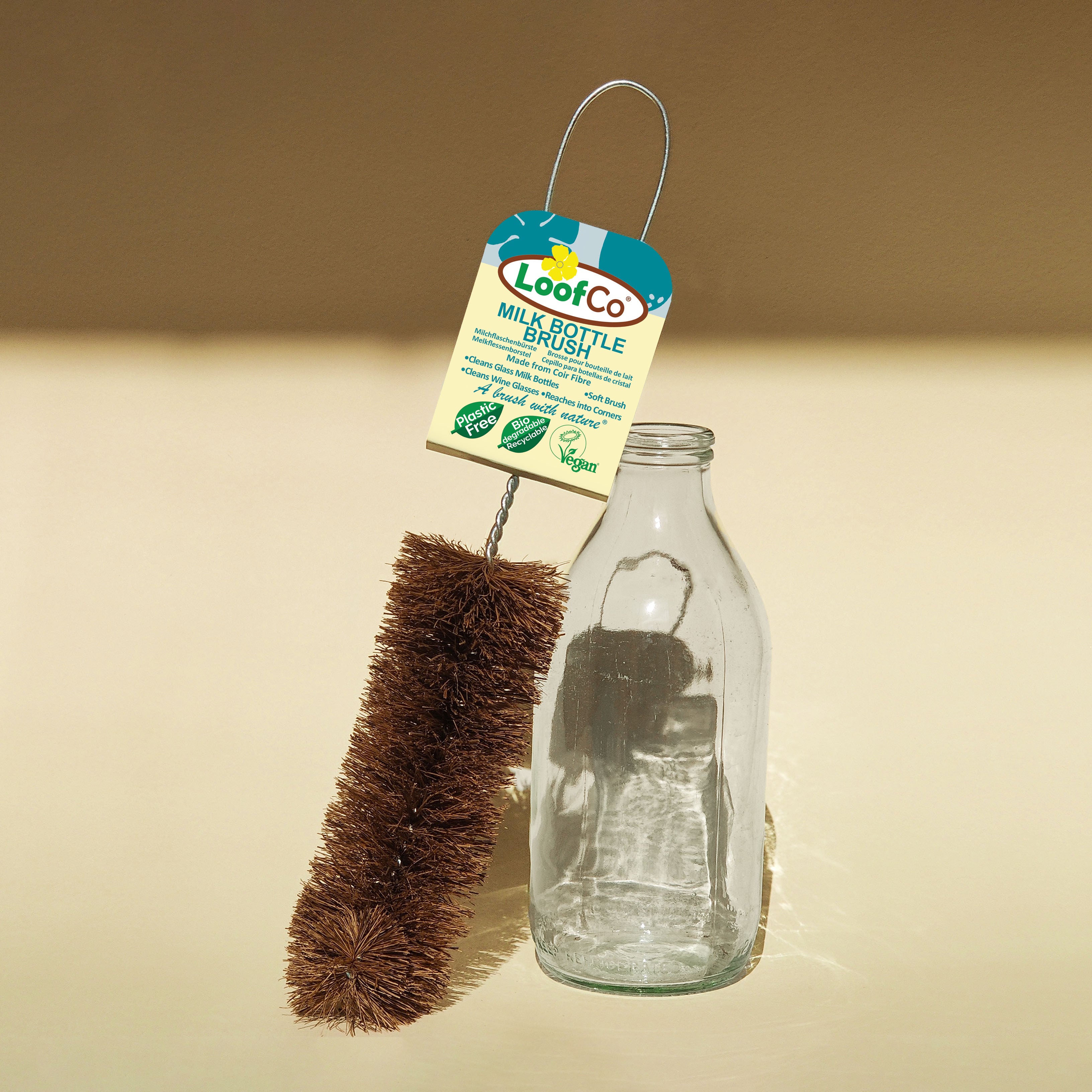 Milk bottle brush with LoofCo label next to a glass bottle on a beige background