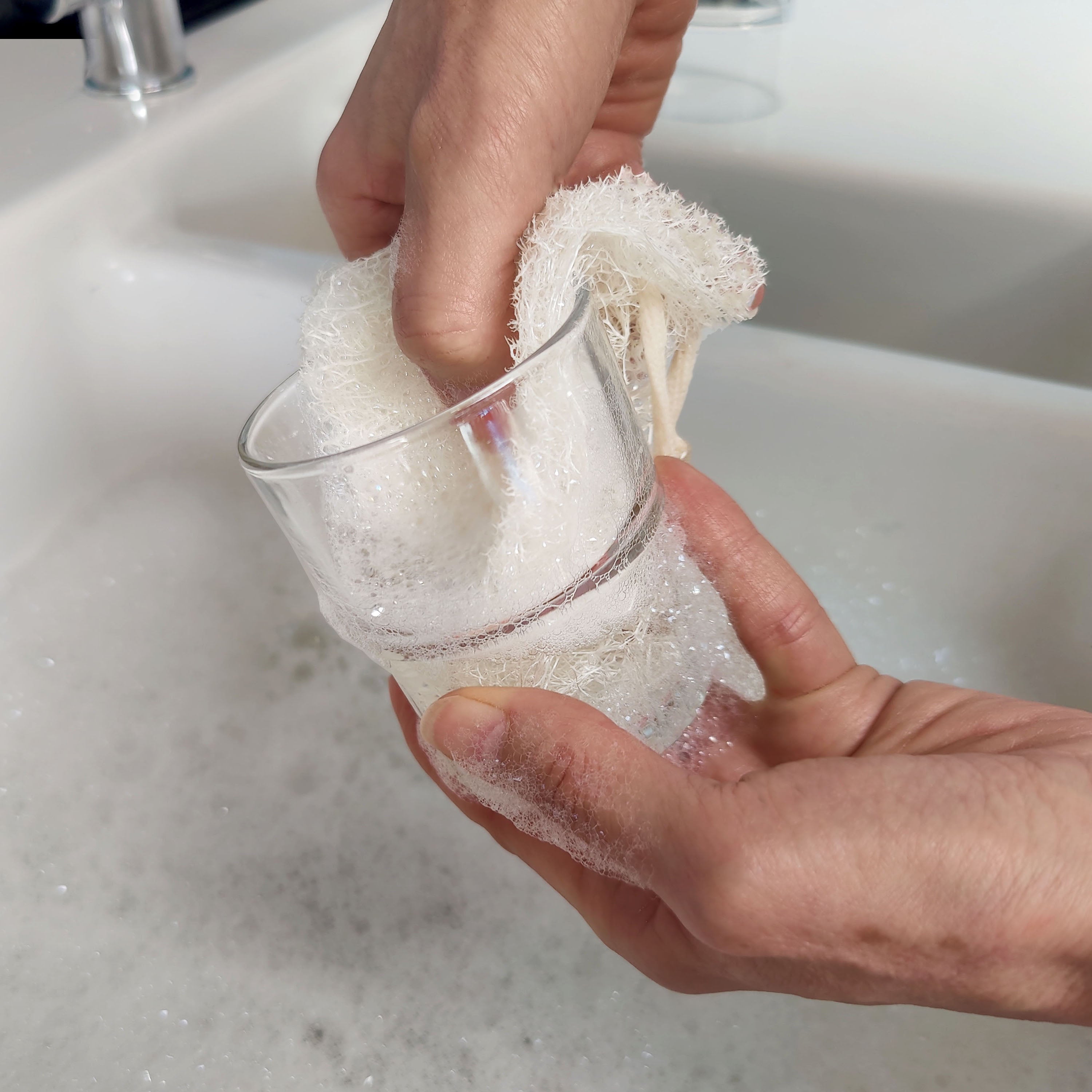 Two hands using LoofCo Slim pad to wash a small drinking glass