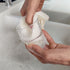Two hands using LoofCo Slim pad to wash a small drinking glass