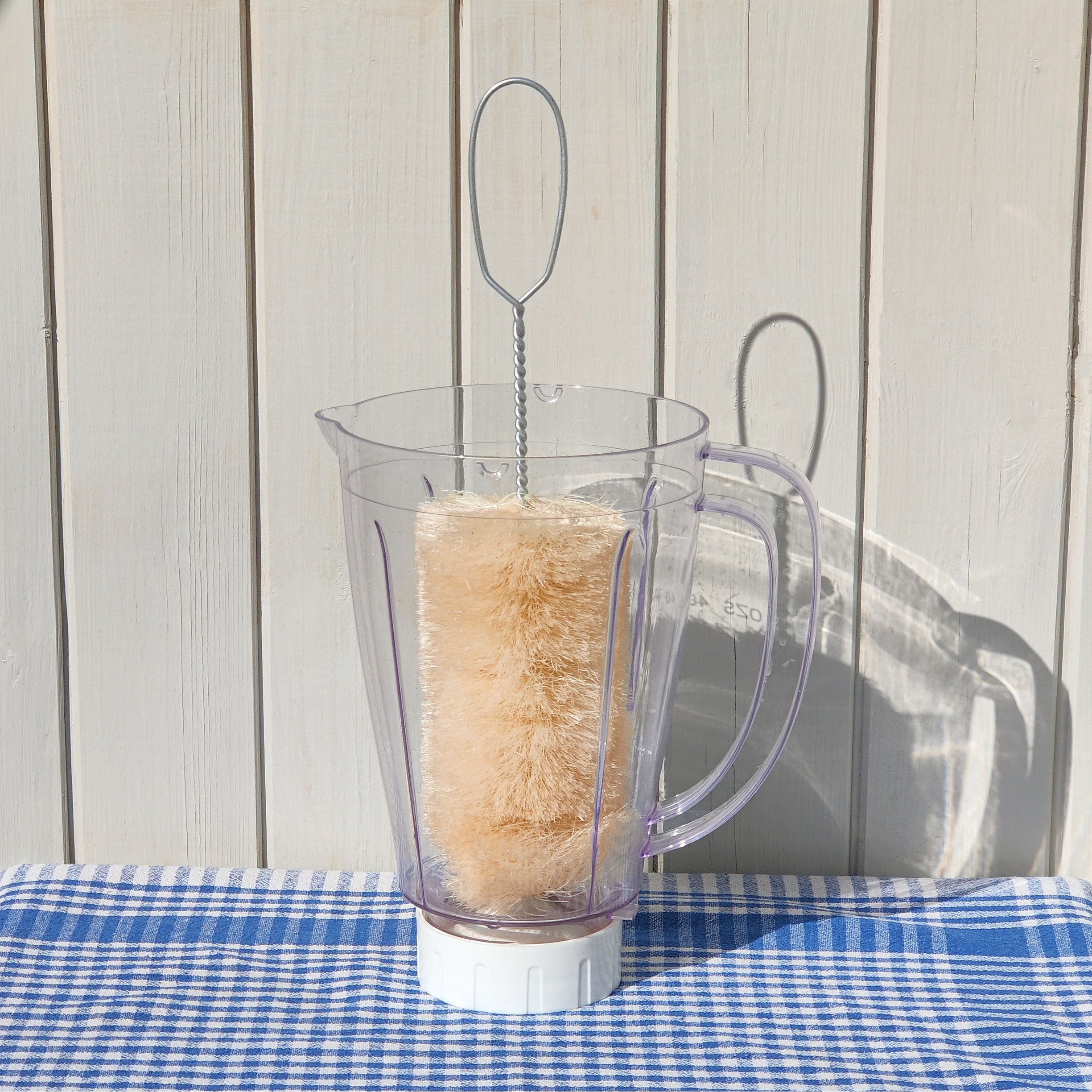 Clear blender jar with a LoofCo Wide Bottle Brush inside on a blue checked tablecloth.