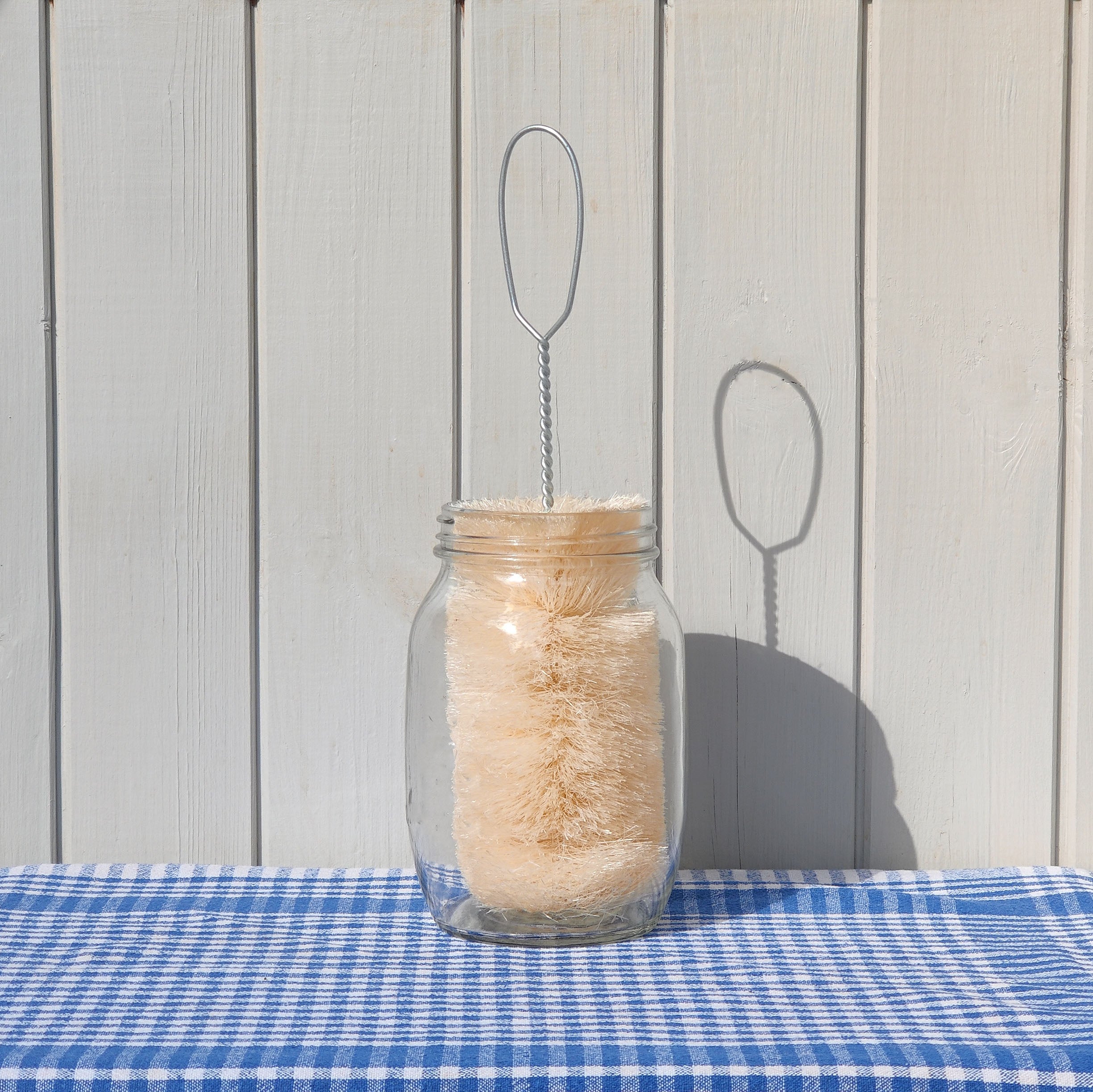 LoofCo Wide Bottle Brush in a mason jar  on a blue checkered tablecloth against a wooden background