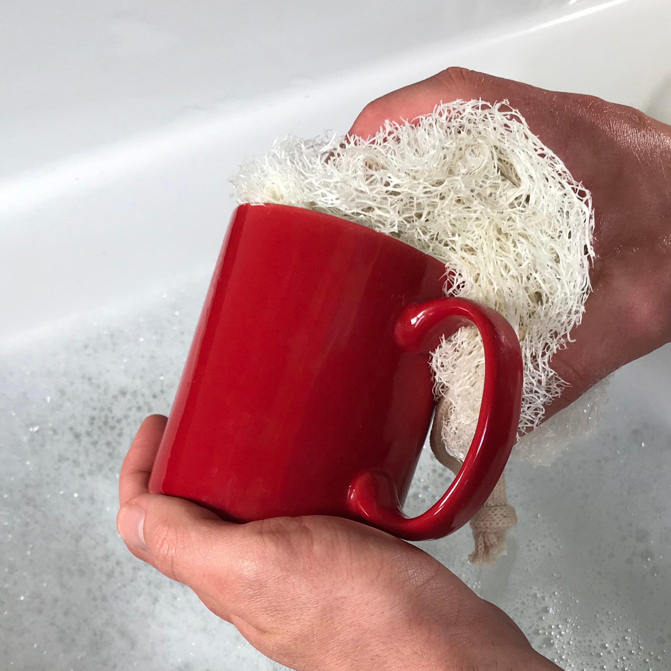 Hand using LoofCo Washing-Up Pad to clean red mug – natural loofah dish sponge in action at sink